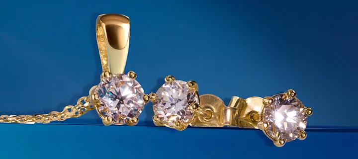 Złota zawieszka i kolczyki z trzema okrągłymi błyszczącymi kamieniami na niebieskim tle