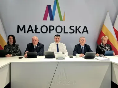 Pięć osób siedzi za białym stołem z tabletami podczas spotkania w sali konferencyjnej z logo Małopolska na ścianie.